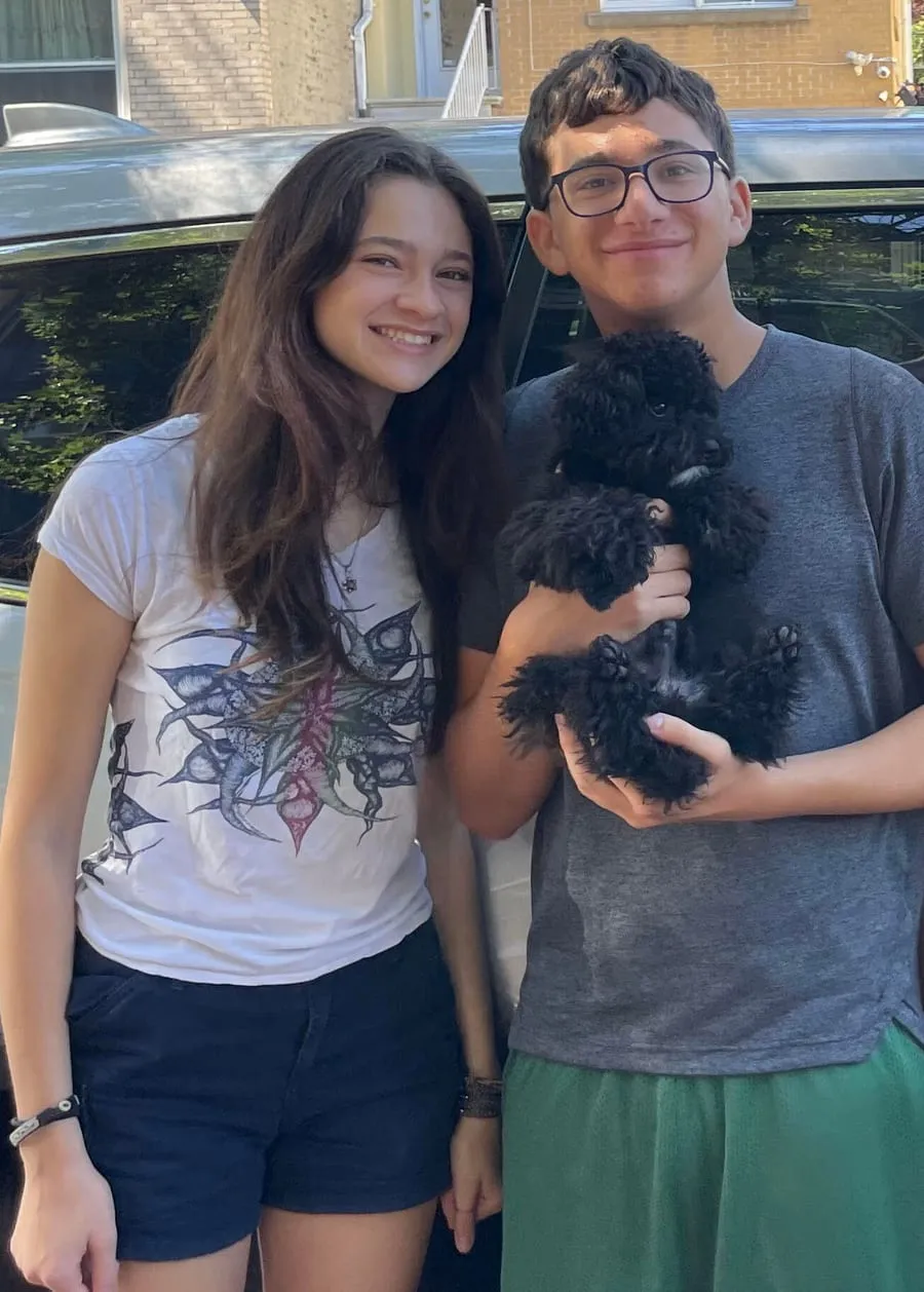 Sophie and Ben, the two teenagers who founded Enable Me Now, standing on a Brooklyn street. Ben is holding a small black dog.